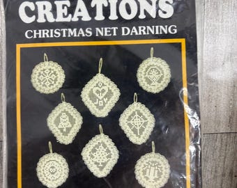 May include: A package of Christmas net darning ornaments. The package is black with a yellow border and features eight cream-colored, intricately designed ornaments. The text "CREATIONS" and "CHRISTMAS NET DARNING" are visible.
