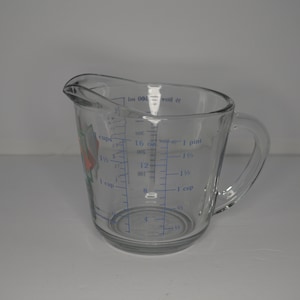 May include: A clear glass measuring cup with a handle. The cup has blue markings for measuring in cups, ounces, and pints. The cup has a floral design on the side.