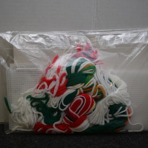 May include: A plastic bag containing a cross-stitch kit with white Aida cloth, red, white, and green embroidery floss, and instructions.