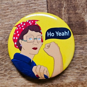 May include: A yellow button with a cartoon image of a woman with red polka dot hair, wearing blue overalls and glasses, with her fist raised in the air. The woman is saying "Ho Yeah!" in a speech bubble.