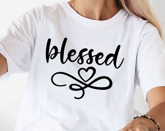 May include: A woman wearing a white t-shirt with the word "blessed" printed on it, holding a black cat in her left hand. She is wearing round sunglasses and a black cat ear headband.