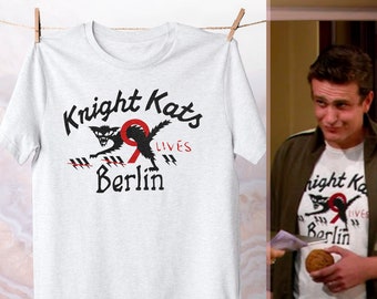 May include: White t-shirt with a black and red graphic print of a cat with the text "Knight Kats 9 Lives Berlin".