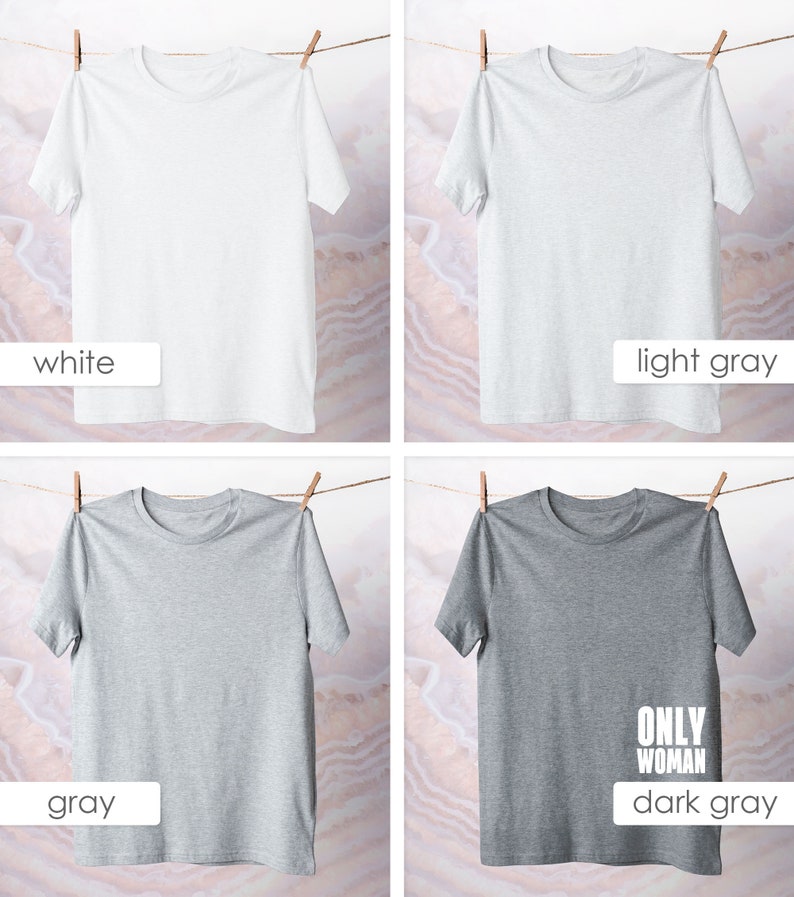 May include: Four t-shirts hanging on a clothesline. The t-shirts are in four different colors: white, light gray, gray, and dark gray. The dark gray t-shirt has the text "ONLY WOMAN" printed on it in white.