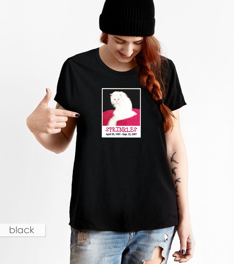 May include: Black t-shirt with a white cat on a pink cushion. The cat is looking to the left. The text "SPRINKLES April 20, 1985 - Sept. 22, 2007" is printed below the cat.