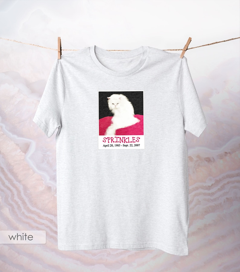 May include: White t-shirt with a photo of a white cat on a pink background. The photo has the text "SPRINKLES" and "April 20, 1985 - Sept. 22, 2007".