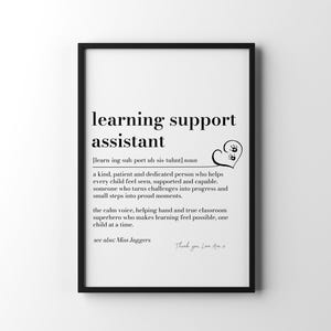 May include: A black framed wall art print featuring a dictionary-style definition of a learning support assistant. The text includes a phonetic pronunciation, a descriptive paragraph, a heart icon with small handprints, and the text see also: Miss Jaggers.