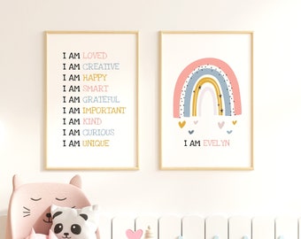 May include: Two framed prints with a rainbow theme. The first print features a rainbow with stars and hearts and the text "I AM EVELYN". The second print features a list of positive affirmations, including "I AM LOVED", "I AM CREATIVE", "I AM HAPPY", "I AM SMART", "I AM GRATEFUL", "I AM IMPORTANT", "I AM KIND", "I AM CURIOUS", and "I AM UNIQUE".