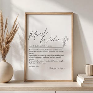 May include: A framed wall art print featuring the dictionary-style definition of the term Miracle Worker in black text on a white background, including phonetic spelling, a noun label, a descriptive paragraph, and the handwritten text Thank you, Love Maya.