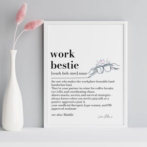 Könnte beinhalten: Ein weiß gerahmter Druck mit dem schwarzen Text "work bestie". Die Definition von "work bestie" ist darunter geschrieben. Links vom Druck befindet sich eine weiße Vase mit rosa Blumen.