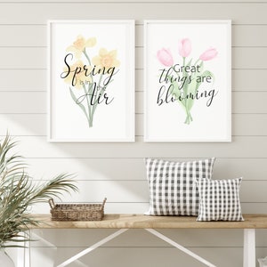 May include: Two framed watercolor prints with floral designs and spring-themed text. The first print features yellow daffodils with the text "Spring is in the air". The second print features pink tulips with the text "Great things are blooming".