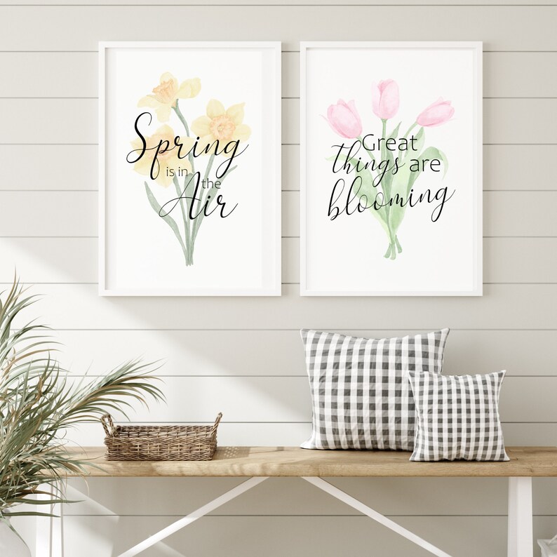 May include: Two framed watercolor prints with floral designs and spring-themed text. The first print features yellow daffodils with the text "Spring is in the air". The second print features pink tulips with the text "Great things are blooming".