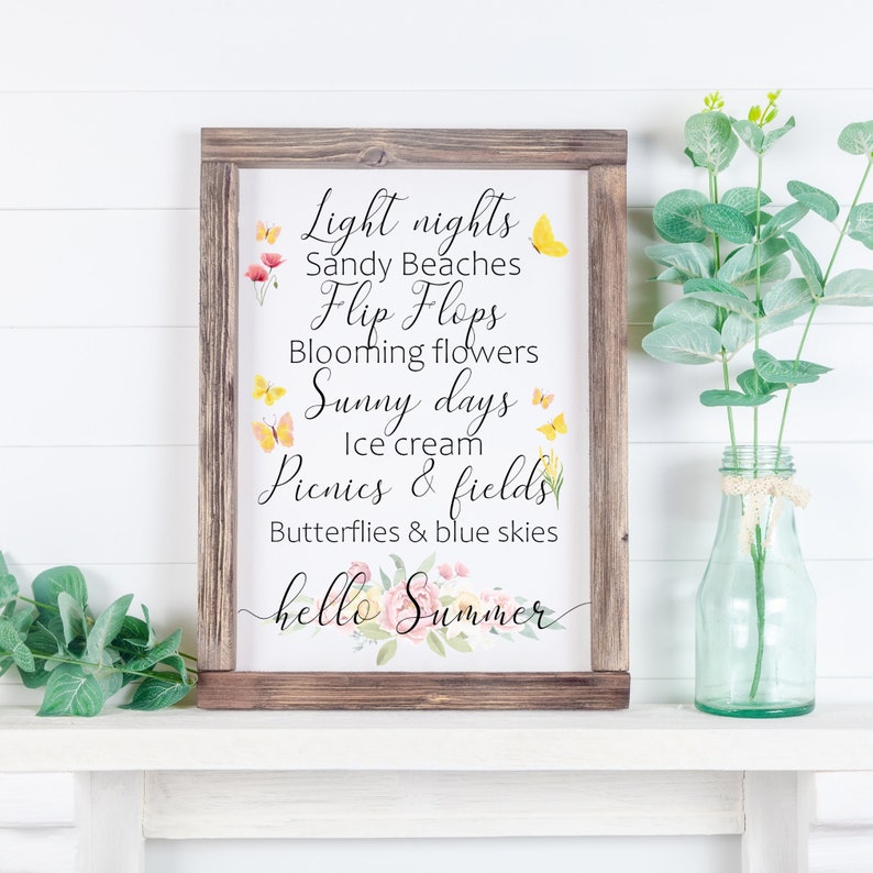 May include: A framed sign with a white background and brown wood frame. The sign features a summer-themed quote with text that reads: "Light nights, Sandy Beaches, Flip Flops, Blooming flowers, Sunny days, Ice cream, Picnics & fields, Butterflies & blue skies, hello Summer". The text is in black and the quote is decorated with watercolor butterflies and flowers.