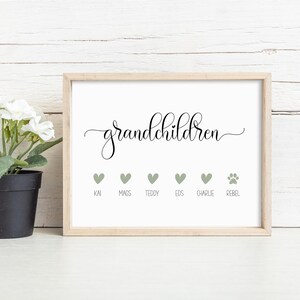 Op de afbeelding: Een ingelijste print met het woord grandchildren in zwarte cursieve letters. Onder de tekst staan vijf saliegroene hartjes en een pootafdruk, elk gelabeld met de namen Kai, Mags, Teddy, Eds, Charlie en Rebel in een eenvoudig zwart lettertype.