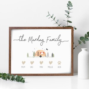 May include: A white framed print with the text "the Mardag Family" in black cursive script. A cartoon illustration of a camper van in a forest setting is above the text. Below the illustration are five icons: four hearts and a paw print. The hearts are labelled "Mum", "Dad", "Max", and "Mollie". The paw print is labelled "Rexi".