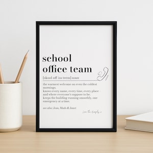 Pode incluir: Uma impressão emoldurada em preto com as palavras "school office team" e uma definição. A definição descreve as funções da equipe, acompanhada por um gráfico de telefone e coração. A impressão está em uma superfície de madeira.