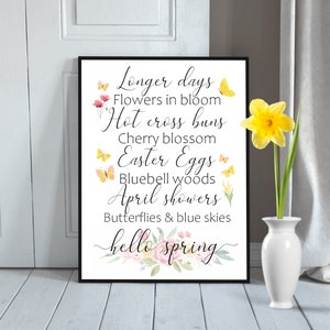 May include: A printable wall art design with a watercolor floral border and the text "Longer days, Flowers in bloom, Hot cross buns, Cherry blossom, Easter Eggs, Bluebell woods, April showers, Butterflies & blue skies, hello spring".