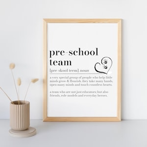 K&ouml;nnte beinhalten: Gerahmter Druck mit den Worten "pre-school team" in schwarzer Schrift. Die Definition des Begriffs steht unter dem Titel. Eine Herzform mit Handabdr&uuml;cken befindet sich rechts vom Text. Eine beige Vase mit Trockenblumen befindet sich im Vordergrund.