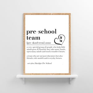 K&ouml;nnte beinhalten: Ein gerahmter Druck mit dem Text "pre-school team" in Schwarz. Die Definition des Begriffs steht unter dem Titel, zusammen mit einem herzf&ouml;rmigen Grafik mit Handabdr&uuml;cken. Der Druck wird auf einem wei&szlig;en Regal mit dem Text "Duridge Pre School" pr&auml;sentiert.