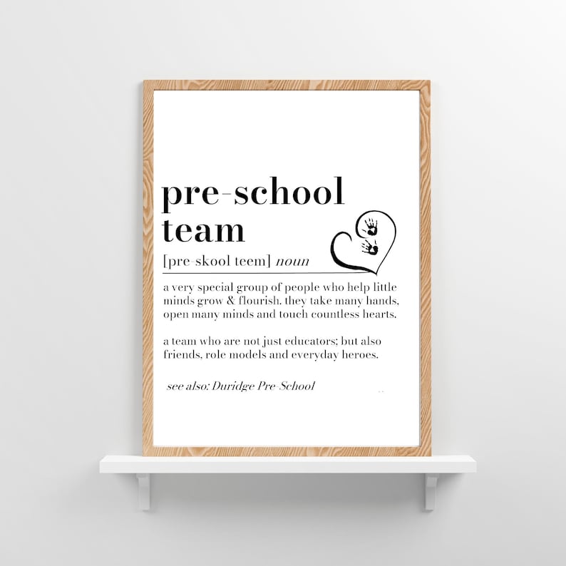 K&ouml;nnte beinhalten: Ein gerahmter Druck mit dem Text "pre-school team" in Schwarz. Die Definition des Begriffs steht unter dem Titel, zusammen mit einem herzf&ouml;rmigen Grafik mit Handabdr&uuml;cken. Der Druck wird auf einem wei&szlig;en Regal mit dem Text "Duridge Pre School" pr&auml;sentiert.