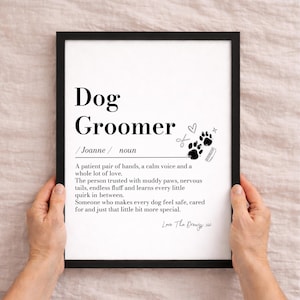 Puede incluir: Una impresión enmarcada en negro que presenta la definición estilo diccionario de un peluquero canino. El texto incluye el nombre Joanne, una descripción de la profesión e ilustraciones negras de un corazón, tijeras, huellas y un peine.