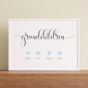 Op de afbeelding: Een wit ingelijste print met het woord grandchildren in zwarte cursieve letters met een klein hartje boven de letter i. Onder de tekst staan vier lichtblauwe hartjes, elk geplaatst boven de namen Poppy, Faith, Kieran en Noah.