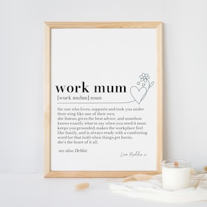 Puede incluir: Un cartel enmarcado con las palabras "work mum" en negro. La definición describe a una persona de apoyo. Un diseño de corazón floral está en la esquina superior derecha. Una vela está frente al marco.