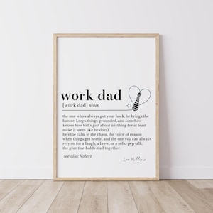 Può includere: Una stampa incorniciata con le parole "work dad" in nero. La definizione di "work dad" è scritta sotto il titolo. Un cravatta e una stella sono disegnate sopra la definizione. La stampa è in una cornice di legno.