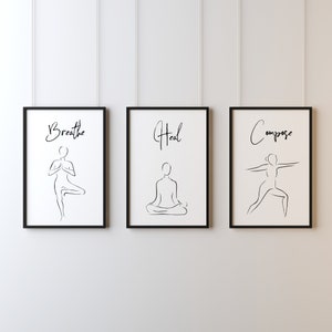 Op de afbeelding: Drie zwarte ingelijste prints met witte achtergronden en zwarte lijntekeningen van yogaposes. De prints hebben de woorden "Breathe", "Heal" en "Compose" boven de poses geschreven.
