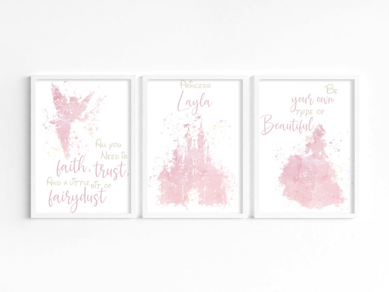 May include: Three pink watercolor prints with white frames. The left print features a pink fairy with the text "All you need is faith, trust, and a little bit of fairy dust". The middle print features a pink castle with the text "Princess Layla". The right print features a pink princess with the text "Be your own type of beautiful".