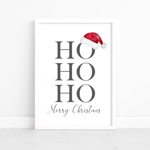 Puede incluir: Una impresi&oacute;n enmarcada en blanco con las palabras "HO HO HO Feliz Navidad" en texto gris. Un gorro de Pap&aacute; Noel rojo con ribete blanco est&aacute; en la parte superior de la impresi&oacute;n.