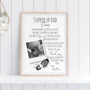 May include: Black and white printable art print with a photo of a father holding a baby. The text reads "Stepped Up Dad Steve" and includes a poem about a stepdad. The print also includes two black footprints.