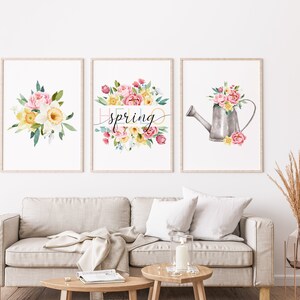 May include: Three watercolor prints featuring floral arrangements with a spring theme. The center print features the text "hello spring" in a colorful font. The left print shows a bouquet of pink and yellow flowers. The right print shows a watering can filled with flowers.