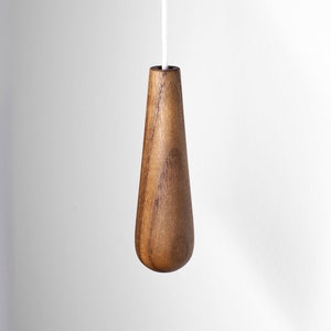May include: A wooden light pull in the shape of a teardrop. The pull is made from dark brown wood and has a smooth finish.