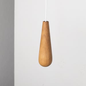 May include: A wooden light pull shaped like a teardrop. The pull is light brown and has a smooth finish.
