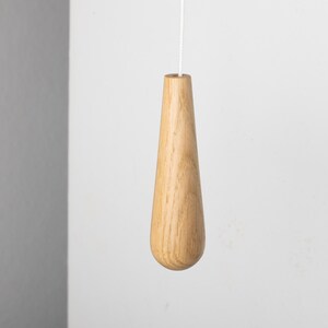 May include: A wooden light pull in the shape of a teardrop. The pull is made from natural wood and has a smooth finish.