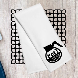 May include: White kitchen towel with a black silhouette of a coffee pot and the text "Pot Head".