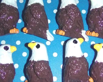 May include: Eight small bald eagle figurines arranged in two rows. Each eagle features a white head, a dark brown body with textured feather details, a bright yellow beak, and orange feet. The eagles are depicted in a seated, upright position.