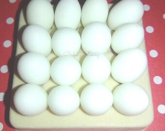 May include: A close-up of a tray with sixteen white, egg-shaped candies. The candies are arranged in four rows of four on a light yellow rectangular base. The background is a red surface with white polka dots.