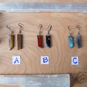 May include: Three pairs of dangle earrings with different coloured stone pendants. The earrings are labelled A, B, and C. The stones are tiger's eye, red jasper, and labradorite.