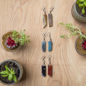 May include: Three pairs of earrings with star-shaped charms and different coloured stone pendants. The stones are brown, blue and red.