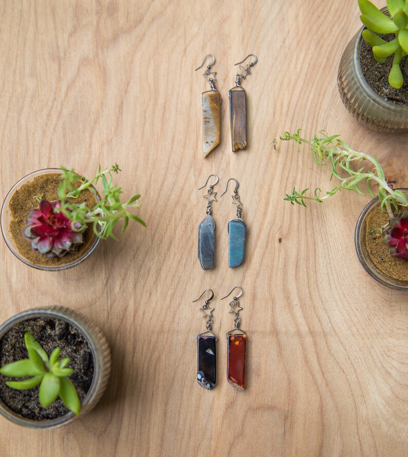 May include: Three pairs of earrings with star-shaped charms and different coloured stone pendants. The stones are brown, blue and red.