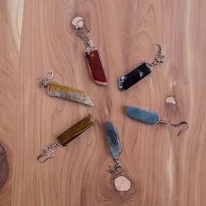 May include: Six pairs of earrings with different coloured stone accents. The earrings are made of metal and have a simple design. The stones are all rectangular in shape and are set in a silver tone metal.