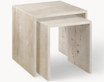 Puede incluir: Un juego de dos mesas nido de color beige claro. Las mesas están hechas de un material similar a la piedra y tienen forma rectangular. La mesa más grande es un bloque sólido, mientras que la más pequeña tiene forma de U.
