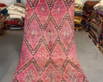 May include: A pink and black Moroccan rug with a diamond pattern. The rug has a fringe border and is made of wool.