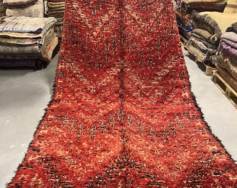May include: A red and black Moroccan rug with a geometric pattern. The rug has a fringe border and is made of wool.