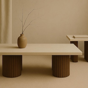May include: A light-coloured rectangular coffee table with two cylindrical, ribbed brown legs. A smaller square side table with similar legs is in the background. A vase with branches sits on the coffee table.