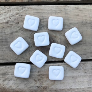 May include: Ten white ceramic square tiles with a raised heart design.