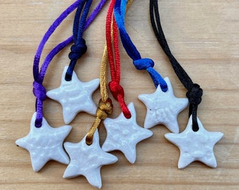May include: Six white ceramic star charms on colourful cords. The cords are purple, dark blue, red, gold, and black.
