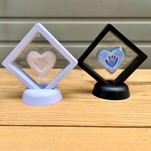 Puede incluir: Dos recuerdos en forma de coraz&oacute;n, uno rosa y otro azul, cada uno encerrado en una caja de exhibici&oacute;n transparente. El coraz&oacute;n rosa presenta una huella de mano, mientras que el coraz&oacute;n azul tiene un dise&ntilde;o de huella de mano. Las cajas de exhibici&oacute;n tienen un marco blanco y negro.