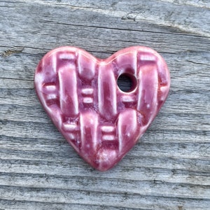 May include: A pink ceramic heart with a woven pattern and a hole in the center.